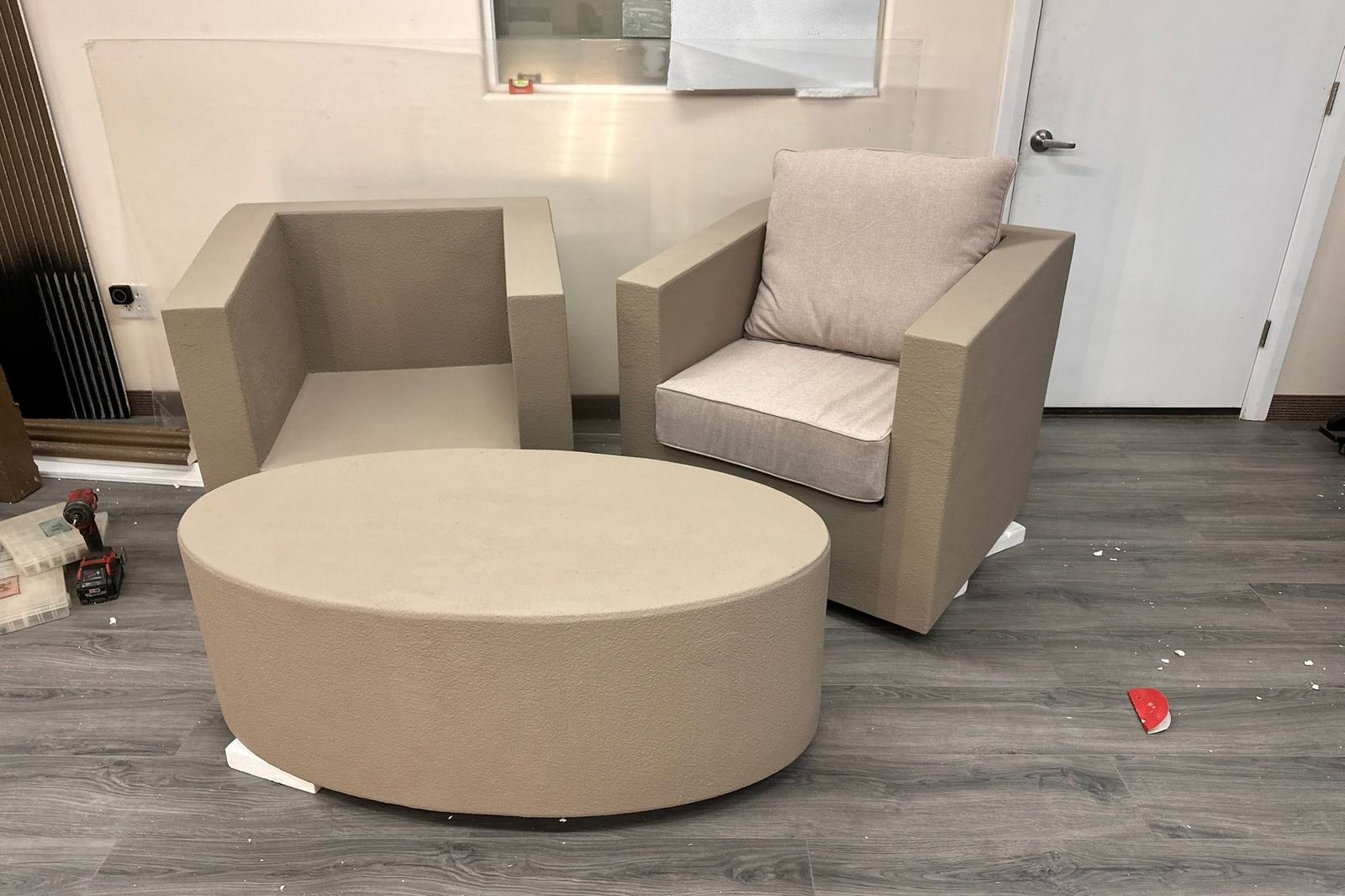 A foam chair frame and round table blank in the shop beside a finished upholstered chair