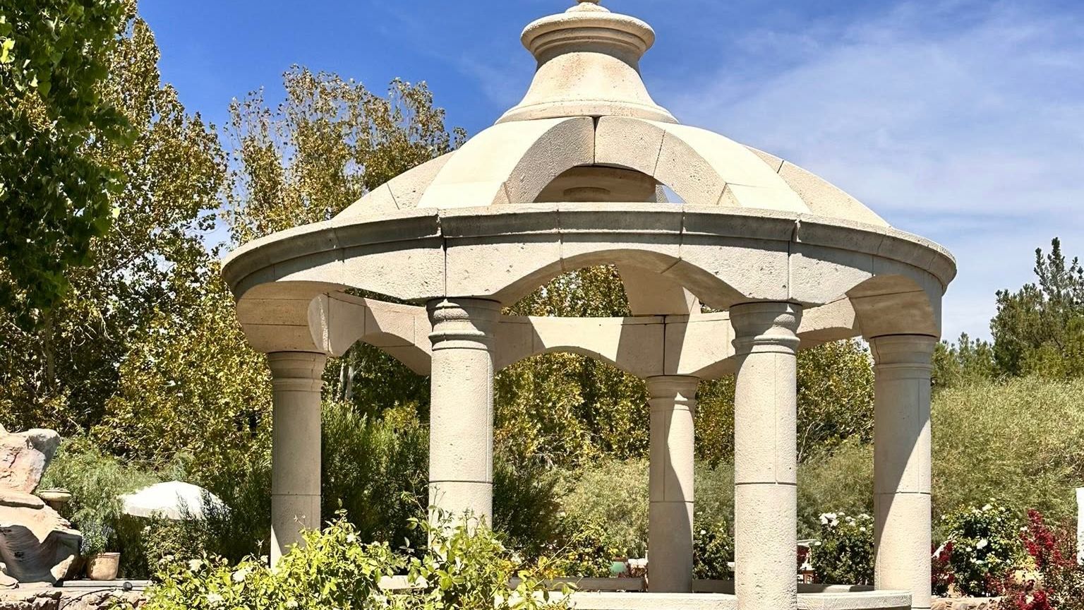 A domed foam gazebo with turned columns and a balustrade standing beside a garden pond